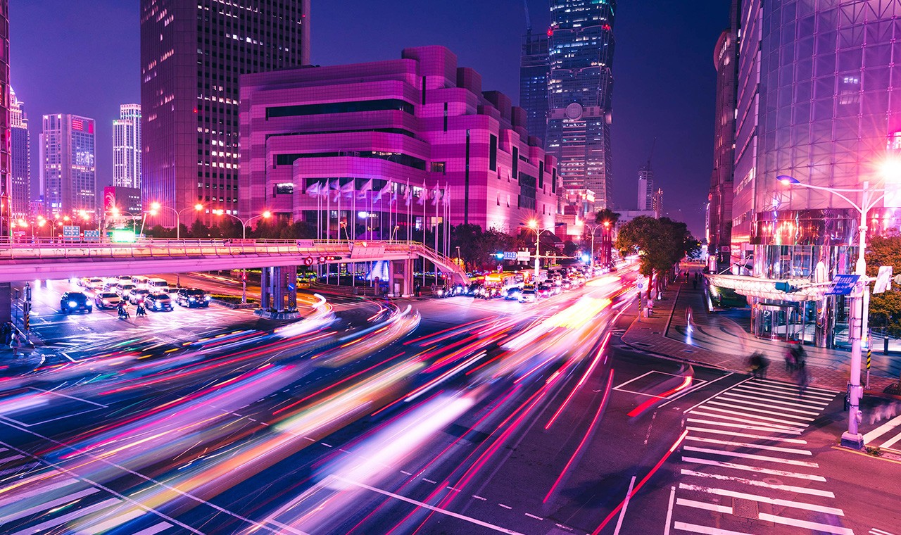 車のライトの光跡が走るライトアップされた高層ビル群の夜景