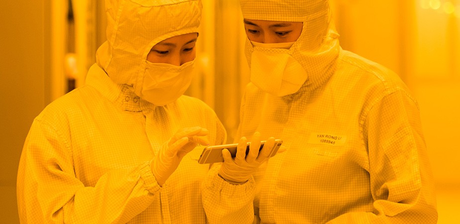クリーンルームスーツを着ている2人のファブ作業員がスマートフォンを見ている