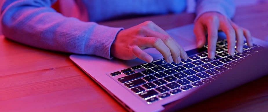 赤と青に光るノートパソコンのキーボードを使用する手のクローズアップ