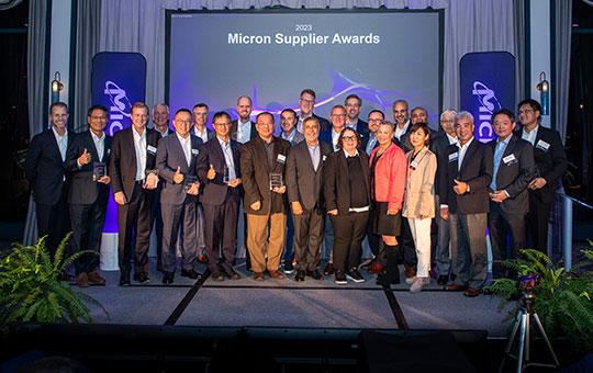 supplier-awards-page-blog-2000x500.jpg：「マイクロンサプライチェーンアワード」と縦のマイクロンバナーの前に立つパートナー